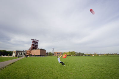 Full length of man flying kite while standing on field against cloudy sky