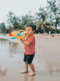 Full length of cute boy holding toy while standing in water