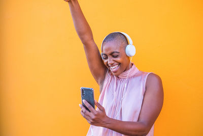 Smiling woman listening music while standing against yellow background