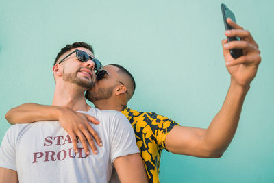 Man taking selfie while kissing boyfriend against wall