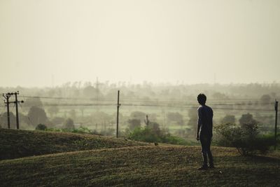 Rear view of man standing on field against sky