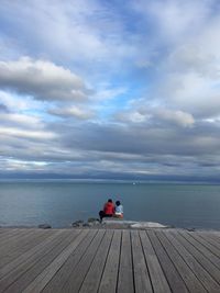 Rear view of couple sitting on sea shore against sky