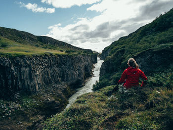 Rear view of young woman standing on cliff against sky