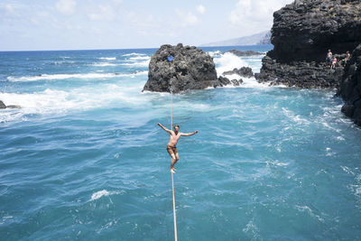 Full length of carefree young man practicing slacklining over sea