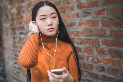 Woman listening music over mobile phone against brick wall