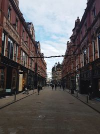People walking on street amidst buildings in city against sky