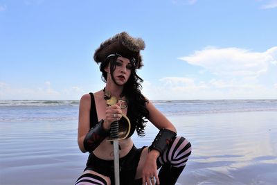 Young woman holding sunglasses on beach against sky