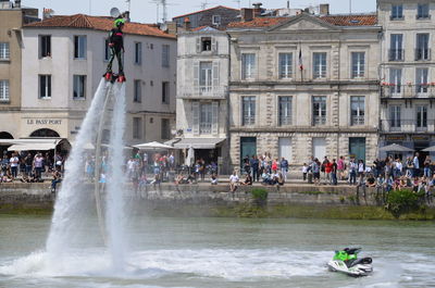 Man flyboarding in sea against building in city