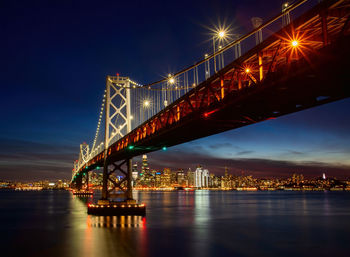 Illuminated bridge over river against sky at night