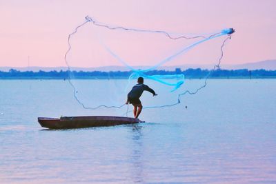 Fisherman with fishing net in sea against sky