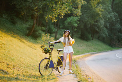 Young beautiful woman standing near yellow bicycle with wicker basket full of flowers 