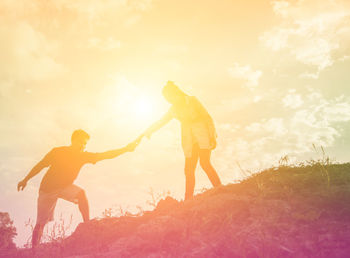 Low angle view of friends standing on land against sky during sunset