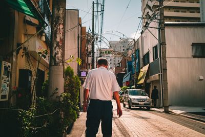 Rear view of man walking on street amidst buildings