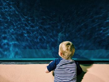 Rear view of boy standing against fish tank in aquarium