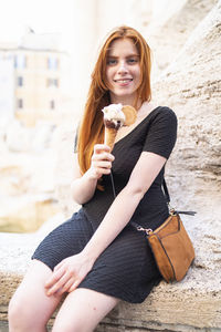 Happy female teenager with ice cream sitting in city