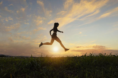 Man jumping on field against sky during sunset