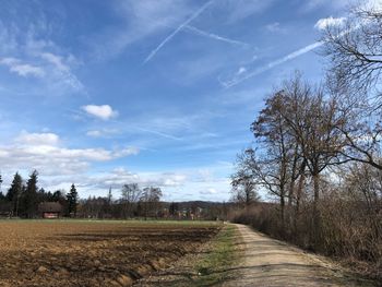 Dirt road amidst agricultural field against sky