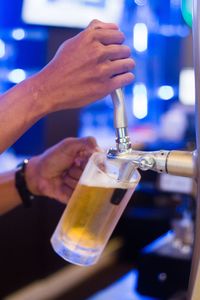 Close-up of cropped hands pouring beer in glass from tap