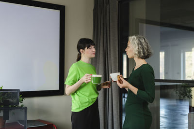Two colleagues in green clothing having a coffee break in office