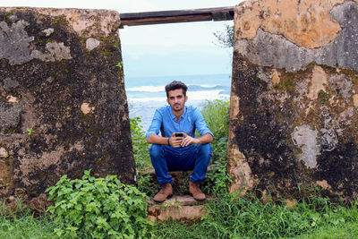 Full length portrait of young man sitting on rock