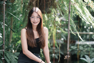 Portrait of young woman standing against trees