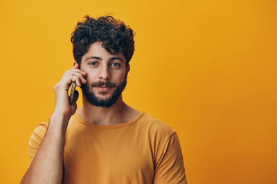 Young man talking on phone against yellow background