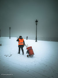 Rear view of man walking on snow covered landscape against sky