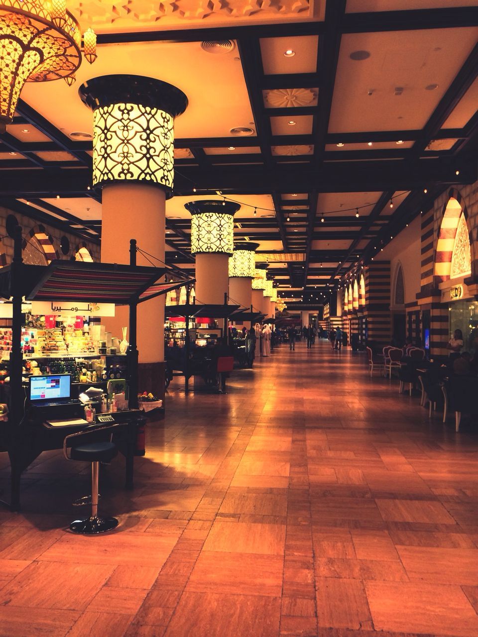 indoors, illuminated, lighting equipment, ceiling, architecture, built structure, flooring, incidental people, tiled floor, architectural column, chair, restaurant, in a row, empty, decoration, retail, table, absence, interior, electric lamp