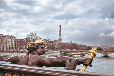 Sculture in a bridge crossing paris city, with the eiffel tower in the background.