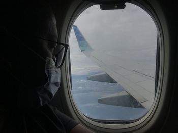 Close-up of man wearing mask looking at airplane wing through window