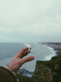 Cropped hand holding feather against sea