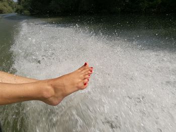 Low section of woman dangling feet over wake in river