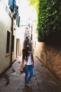 Rear view of woman walking on footpath amidst buildings in city