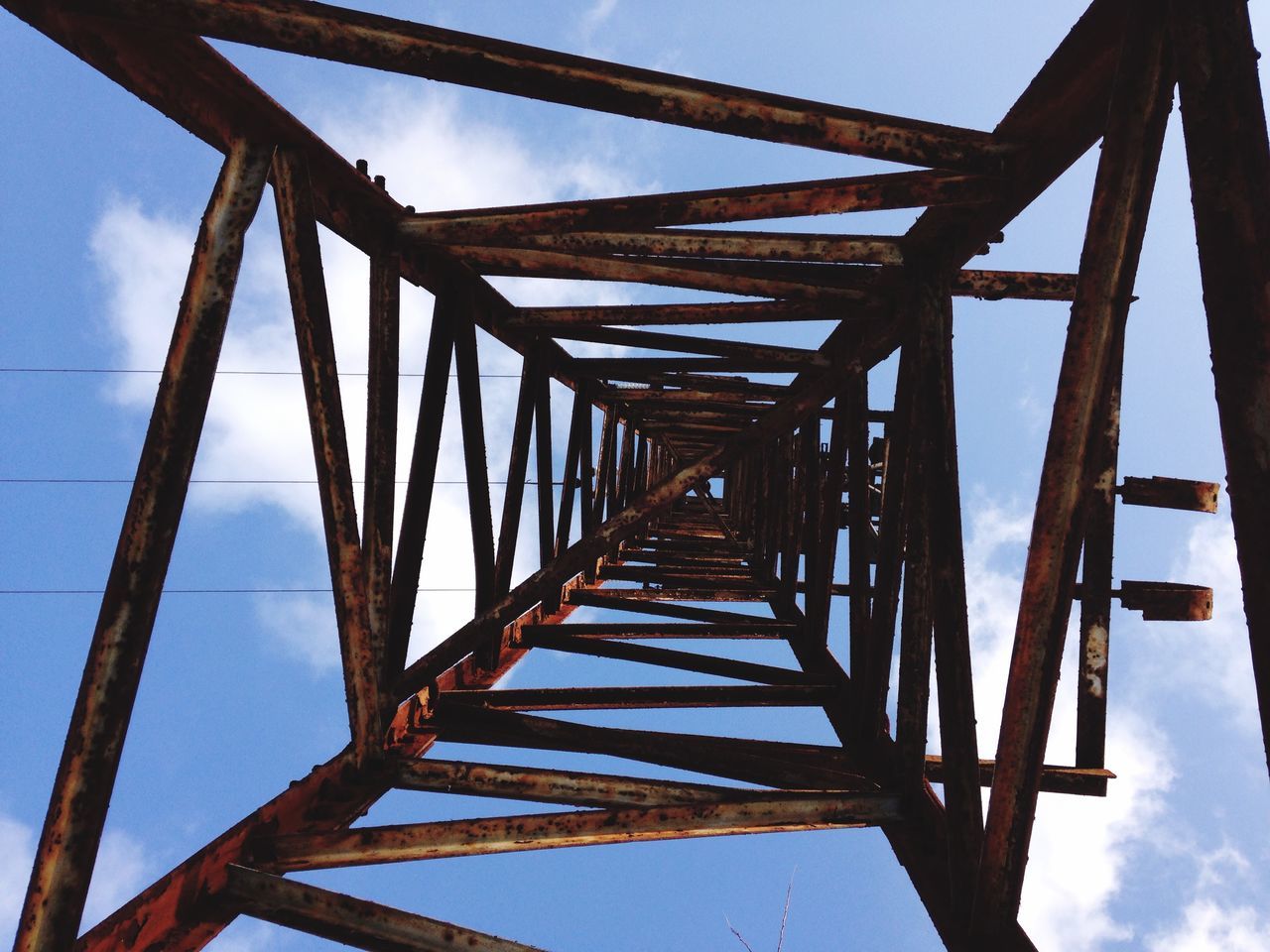 low angle view, connection, built structure, metal, sky, architecture, engineering, metallic, bridge - man made structure, day, bridge, no people, outdoors, blue, clear sky, grid, cloud, support, diminishing perspective, iron - metal