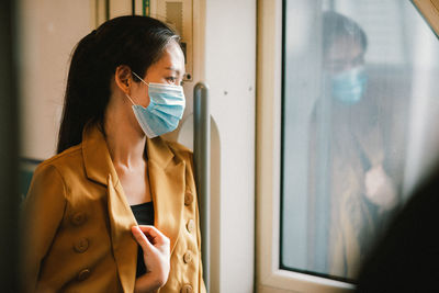 Businesswoman wearing mask looking through window in train