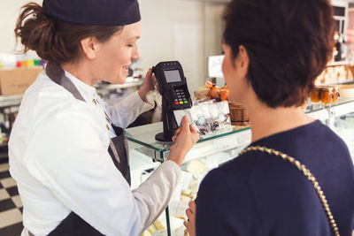 Saleswoman assisting female customer with credit card reader at grocery store