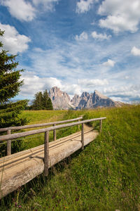 Wooden footbridge at seiser alm hiking trail with sassolungo mountain group against sky