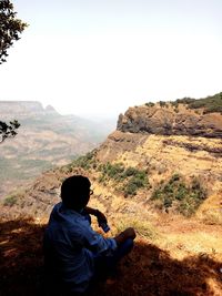 Rear view of woman sitting on mountain against sky