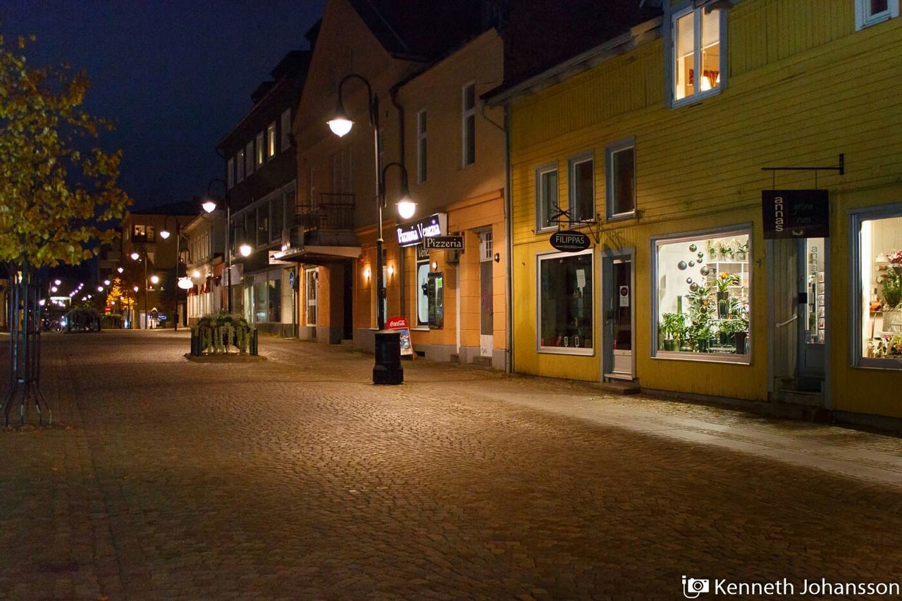 building exterior, illuminated, night, architecture, built structure, city, street, transportation, city life, street light, road, incidental people, building, outdoors, city street, store, text, car, residential structure, residential building