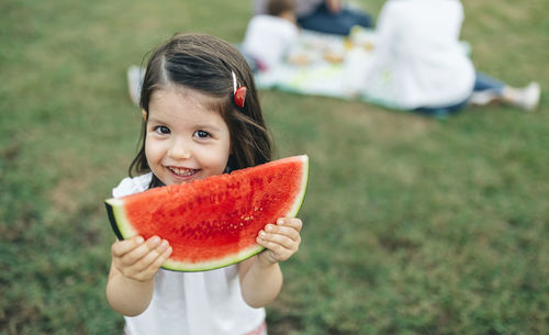 Portrait of smiling girl holding watermelon slice with her family in background