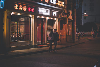 Rear view of man walking on illuminated street at night