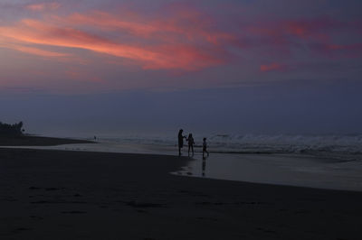 Silhouette people on beach against sky during sunset