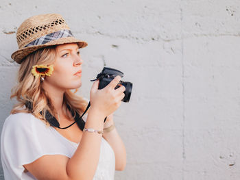 Young woman photographing against wall