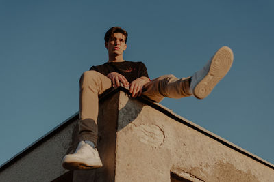 Low angle view of young man sitting against clear blue sky