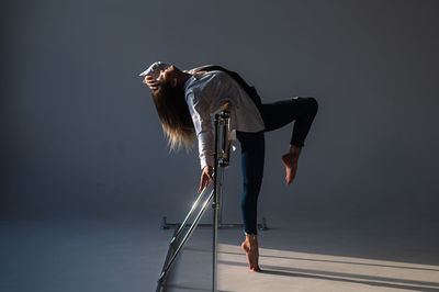 Caucasian woman in casual clothes pulls the split at the ballet barre. 