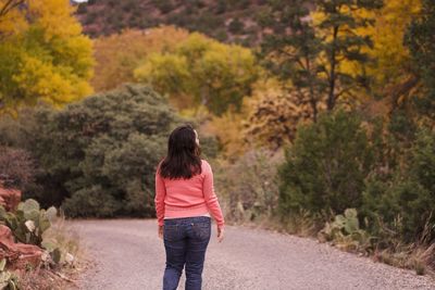 Rear view of woman walking on road amidst trees