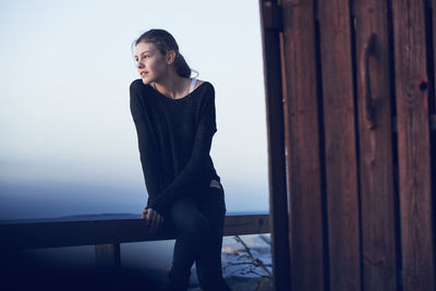 Young woman looking away while standing on wood