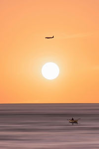 Silhouette airplane flying over sea against orange sky