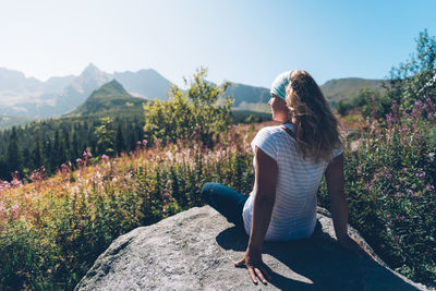 Rear view of woman sitting on rock during sunny day