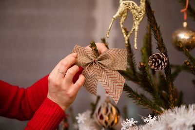 A woman in a red sweater improves a bow hung on a christmas tree.